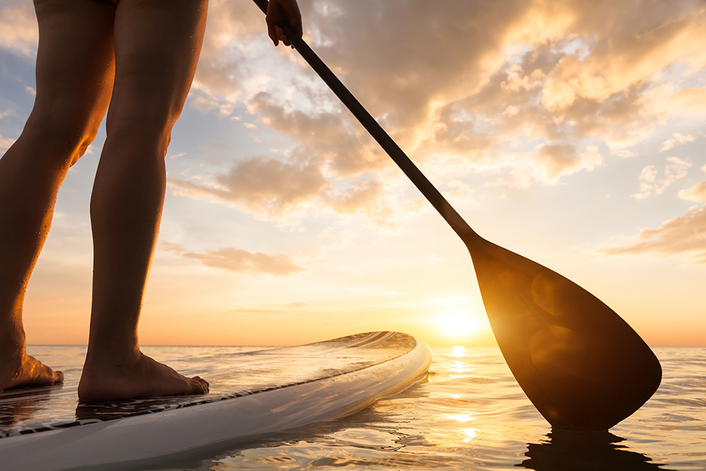 A person stands on a stand-up paddle board on calm water at sunset.
