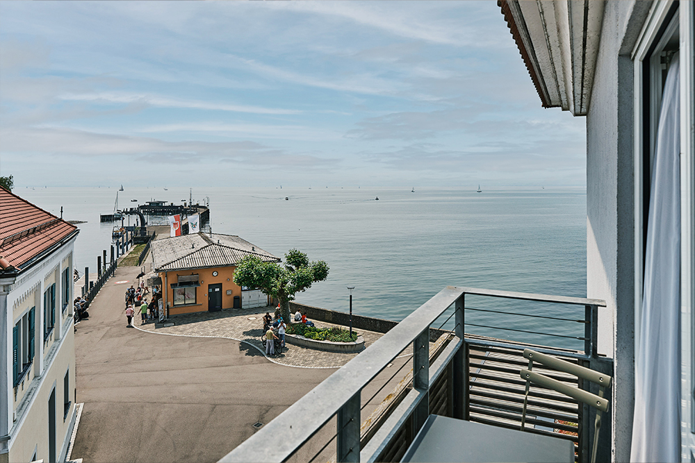 View of Lake Constance, a lakeside promenade and a small harbor from a balcony.