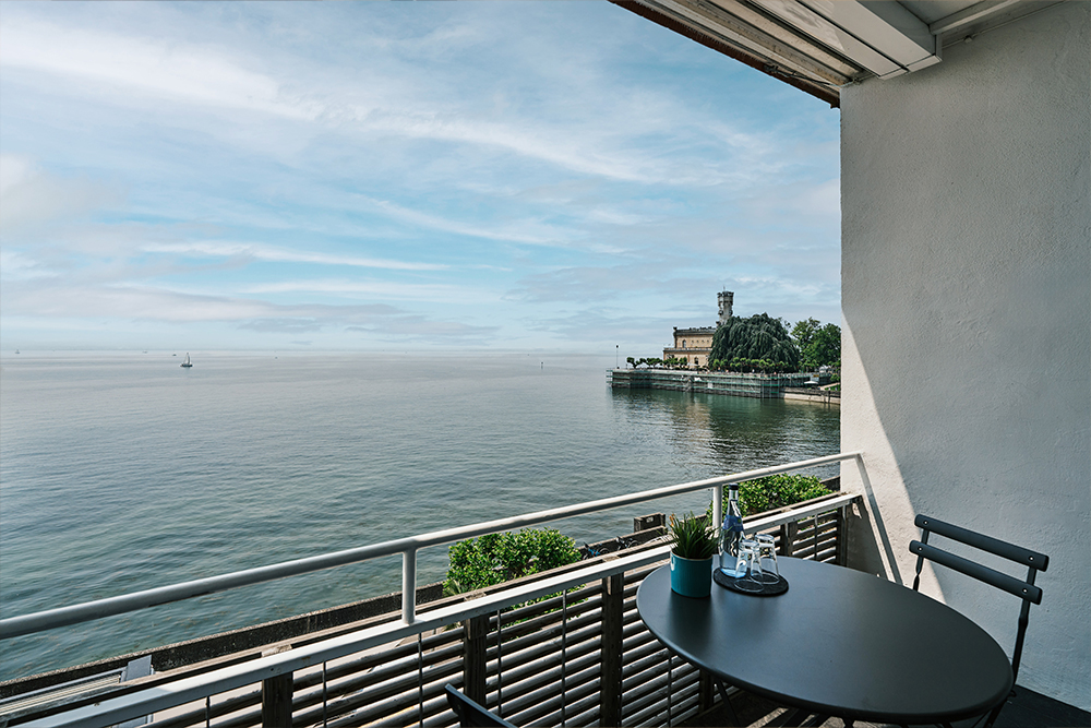 Balcony with table and chairs directly on Lake Constance with a wide view over the calm water.