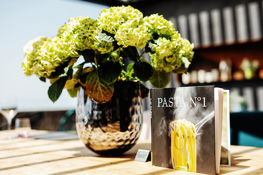 Vase with green hydrangeas and cookbook on a decorated table in a modern setting.