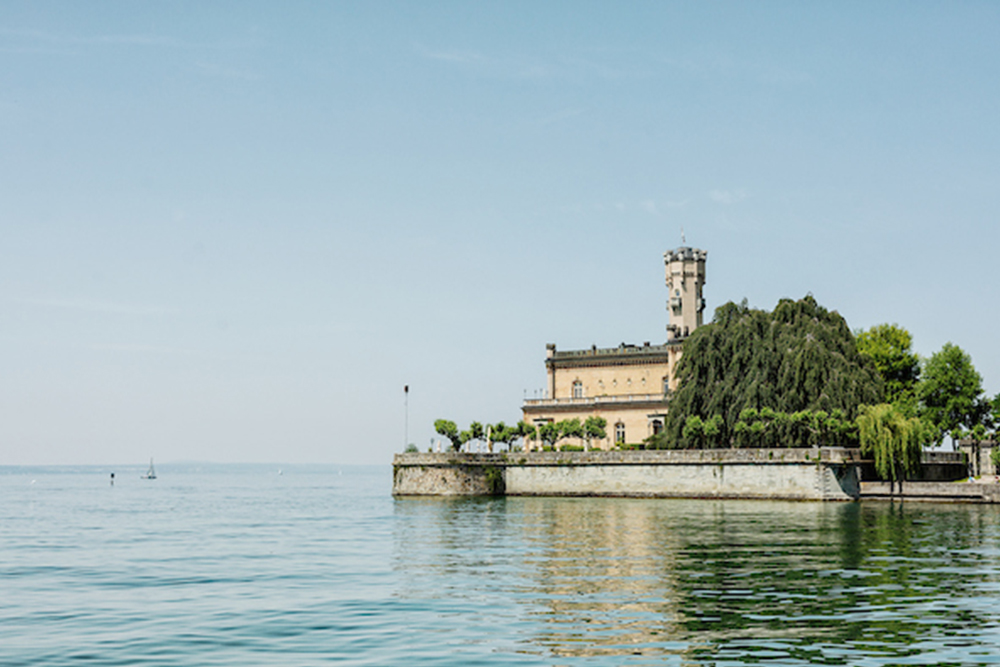 Historic building with observation tower directly on the shores of Lake Constance with calm water and blue skies.