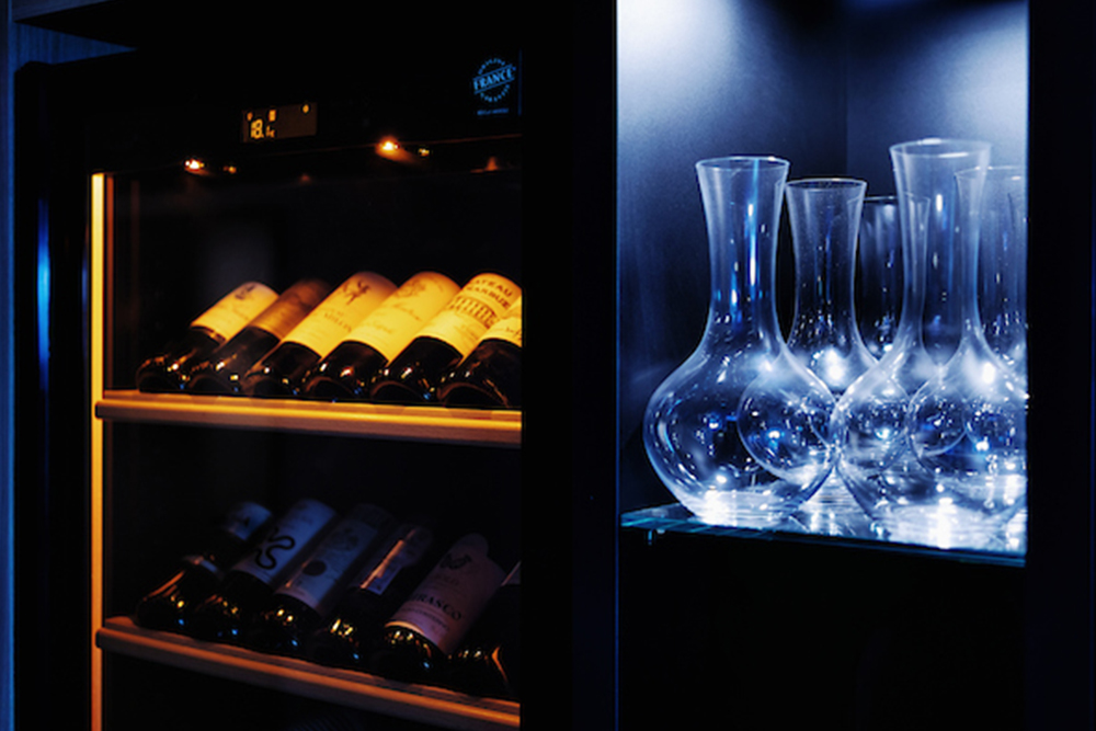 Wine bottles and elegant carafes are illuminated in a modern wine cabinet.