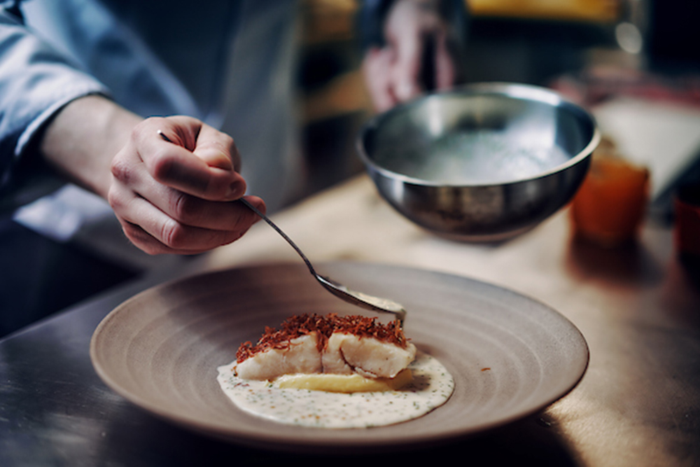 A chef refines an artfully prepared fish dish in a restaurant kitchen.